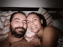 a man with a beard is laying next to a woman who is smiling for the camera