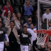 a group of people are watching a basketball game and one of the players is wearing a thunder shirt .