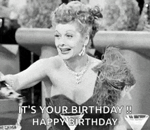 a black and white photo of a woman sitting at a table holding a martini glass and saying it 's your birthday !