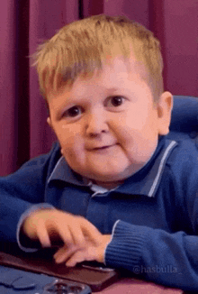 a little boy is sitting at a table with his hands on a keyboard and making a funny face .