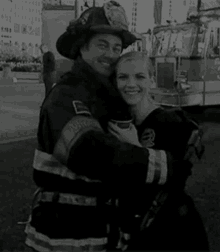 a firefighter and a woman are hugging each other in a black and white photo .