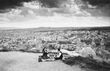 a black and white photo of a man and woman sitting on a blanket on top of a hill overlooking a city