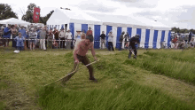 a man without a shirt is mowing grass with a pitchfork in front of a crowd of people and a banner that says awesome