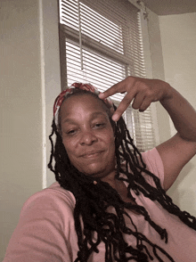 a woman with dreadlocks is making a peace sign in front of a window with blinds