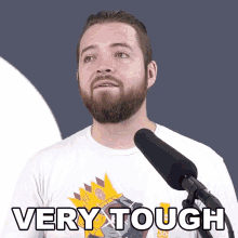 a man with a beard is standing in front of a microphone with the words very tough written on his shirt