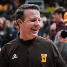 a man wearing an adidas jacket laughs while standing in front of a crowd