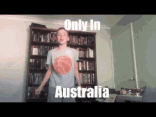 a boy wearing a grey shirt with a basketball on it is standing in front of a bookshelf with the words only in australia on it