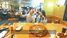 a man and woman sitting at a table with a pizza and a sign that says " crust not included "