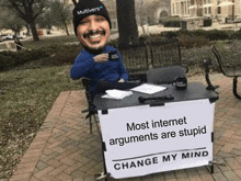 a man sits at a table with a sign that says change my mind