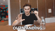 a man sitting at a table with a plate of food and a bottle of water with the word outstanding written on the table