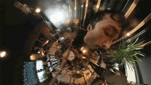 a man is playing drums in a room with a plant in the foreground .