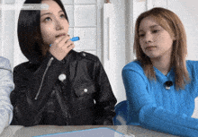 two girls are sitting at a table and one has a blue pen in her mouth