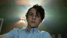 a young man with curly hair wearing a blue shirt is sitting in a dark room .