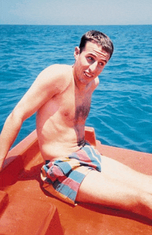 a shirtless man sitting on a boat in the ocean