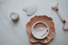 a bowl of pink cream sits on a plate next to a facial roller