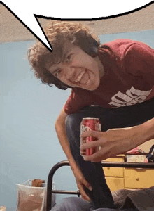 a young man is sitting on a bed holding a can of soda and making a funny face .