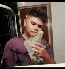 a boy in a purple tie dye shirt is holding a piece of bread in front of his face