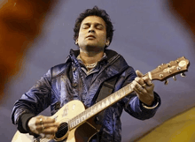 a man in a blue jacket is playing a guitar .