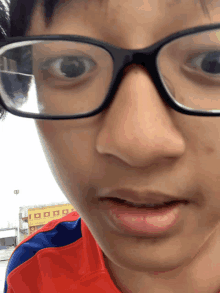 a close up of a person 's face with glasses and a red and blue shirt