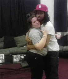 a man and a woman are hugging each other in a living room . the woman is wearing a pink hat .