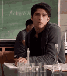 a young man sits at a desk in front of a blackboard that says a + d + v + a on it