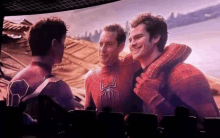 three spider-man are hugging each other in a theater .