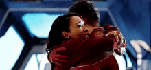 a woman is hugging a man in a red jacket in a room .