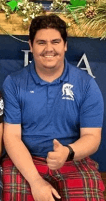 a man wearing a blue polo shirt and a red kilt is giving a thumbs up .