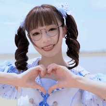 a girl wearing glasses and pigtails makes a heart shape with her hands