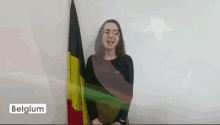 a woman stands in front of a flag with the word belgium on the bottom right