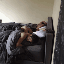 three men sleeping on a bed with grey sheets and pillows