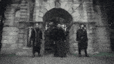 a group of men standing in front of a stone archway with the letter a on it