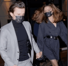 a man and a woman wearing masks are holding hands and walking down the street .