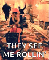 a woman is riding a scooter down a hallway with the words `` they see me rollin '' written on it .