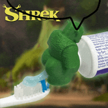 shrek toothpaste is being squeezed onto a toothbrush with a green hand holding it