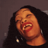 a woman with red lipstick and hoop earrings is laughing with her mouth open