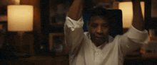a man in a white shirt is sitting in a chair with his arms up in the air .