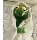 a green stuffed frog is wrapped in a white blanket .