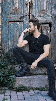 a man in a black shirt is sitting on a set of steps in front of a wooden door