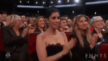 a woman in a black dress is sitting in a crowd of people applauding at an emmy awards show .