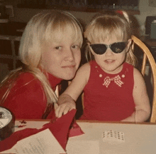 a little girl wearing sunglasses sits next to a woman wearing a red dress