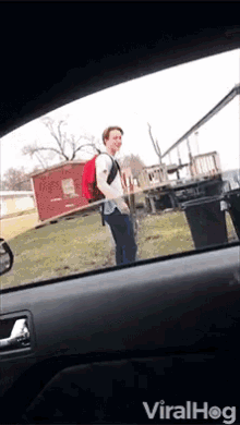 a man with a backpack is standing in front of a red shed with the words viralhog on the bottom