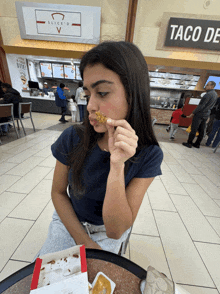 a woman eating a slice of pizza in front of a taco deli