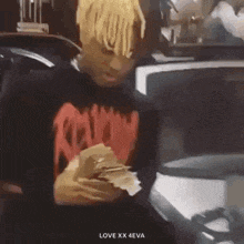 a man with dreadlocks is holding a bunch of money in his hands in front of a car .