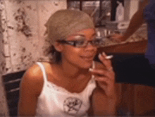 a woman wearing glasses and a head scarf is sitting in a kitchen .