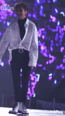 a man in a white shirt and black pants stands on a stage with purple lights behind him and the words fanfan on the bottom