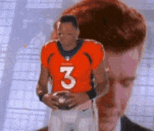 a man in an orange jersey with the number 3 on it holds a football