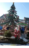 a man in a blue jacket stands next to a statue of santa claus