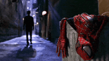 a man is walking down a dark alleyway next to a spider man costume hanging from a wall .