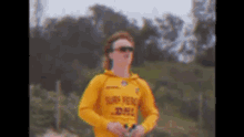 a man wearing sunglasses and a yellow shirt with the word surf on it is standing on a beach .